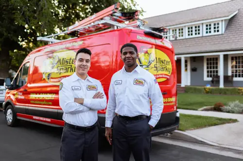 Two Mister Sparky Electrician Techs standing outside of a home and their work van